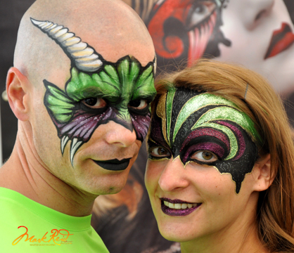 a man and a woman in painted on masks that are purple and lime green his has horns